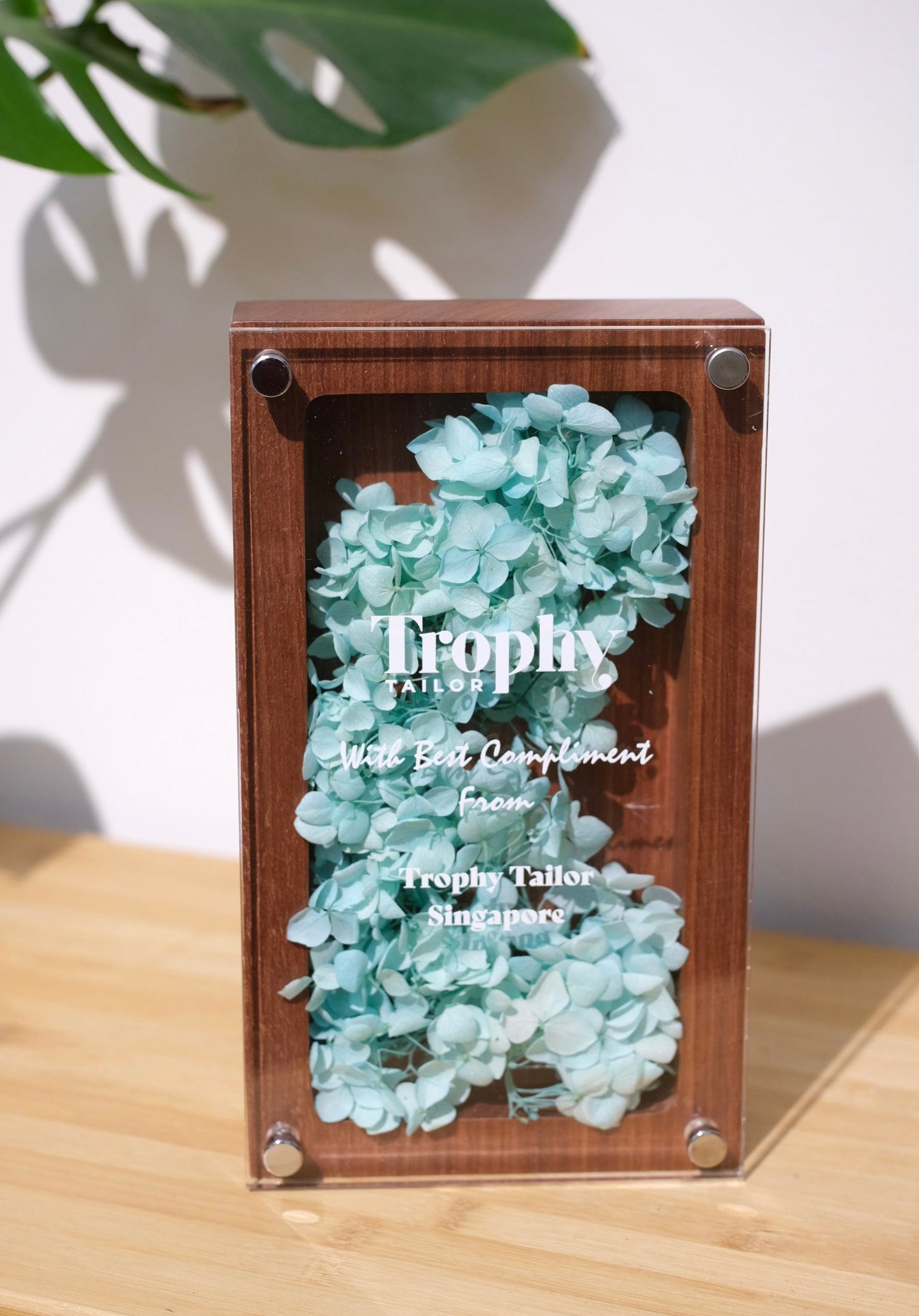 Wooden frame with decorative flowers and 'Trophy Tailor' branding on a wooden surface.