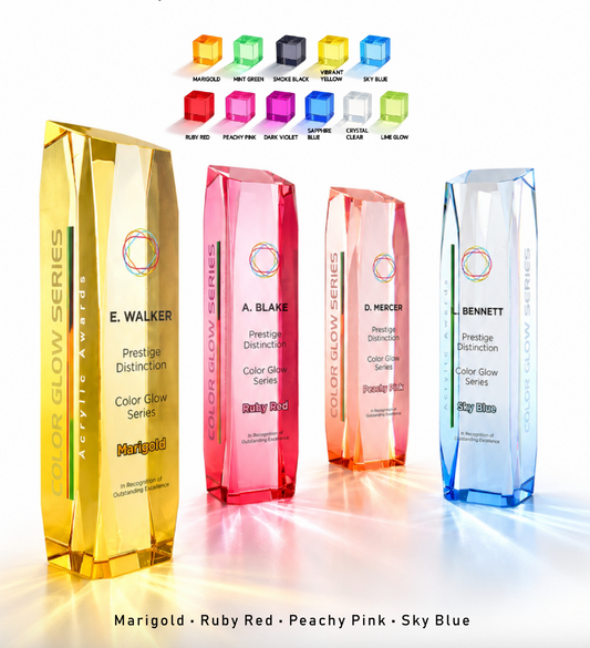 Four faceted acrylic award trophies in different colors are displayed on a reflective white surface: a tall marigold gold trophy, a tall ruby red-pink trophy, a peach-pink trophy, and a tall sky-blue trophy. Above them are smaller color options, and text at the bottom lists the color names.